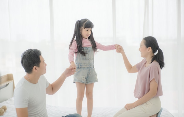 Happy asian family mother, father and daughter on bed in bedroom.