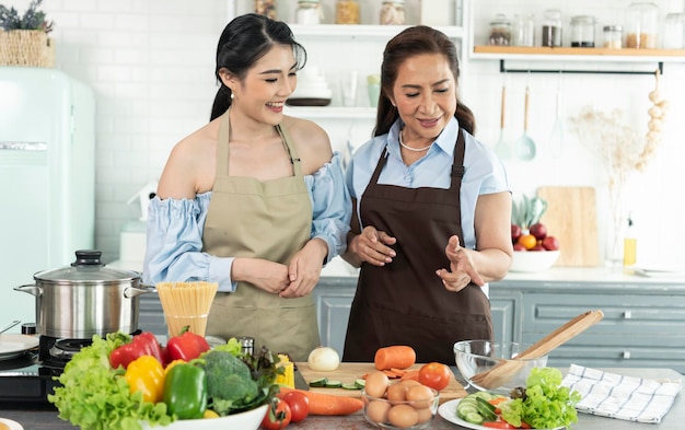 Madre di famiglia asiatica felice che insegna alla figlia a fare l'insalata in cucina a casa