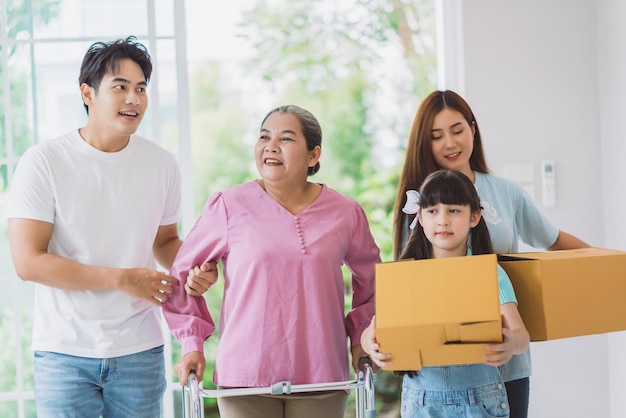 Happy asian family moving to new home young family member\
carrying cardboard box to living room grandmother with fam members\
on moving house day