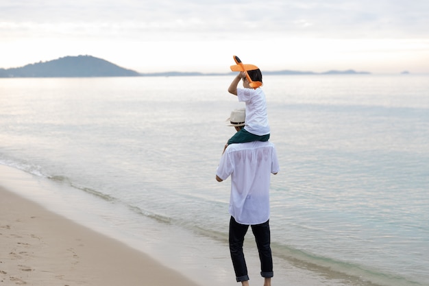 写真 夏休みに幸せなアジア家族父親の息子が一緒に飛んでいる飛行機で遊んでビーチを歩いて朝には、日の出。休日と旅行のコンセプトです。