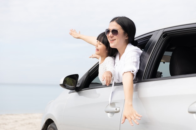 Photo happy asian family on summer vacation mother and daughter open arms playing plane flying together in car on the beach. holiday and car travel concept.