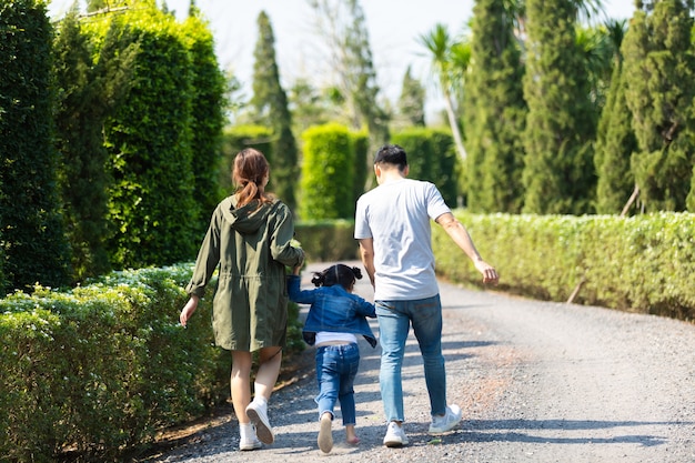 Foto felice famiglia asiatica che cammina e si tiene per mano insieme ai bambini nel parco. felice padre di famiglia madre e figlia figlia