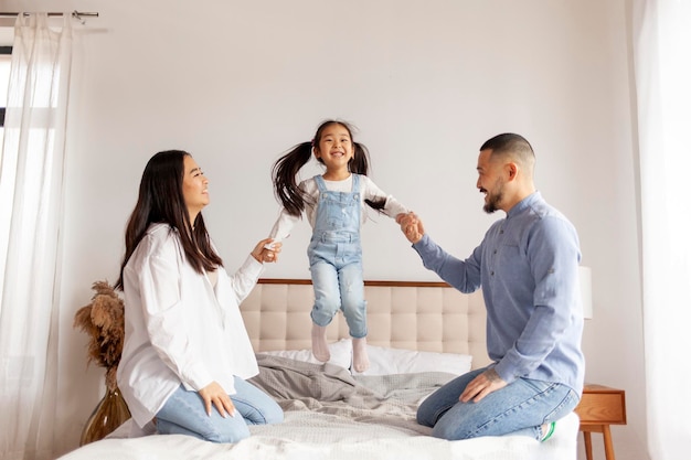 happy asian family with daughter play and rejoice at home on the bed little korean girl jumping