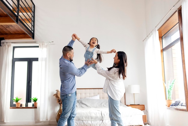 Счастливая азиатская семья с маленькой дочерью стоит дома в спальне и радуется папе и маме