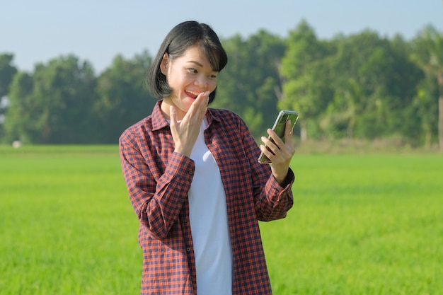 緑の農場でうれしいすごい驚きの顔でスマートフォンを探している幸せなアジアの農家の女性