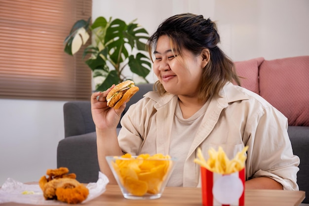 행복한 아시아 뚱뚱한 여성은 거실에서 맛있는 햄버거를 즐겨 먹는다