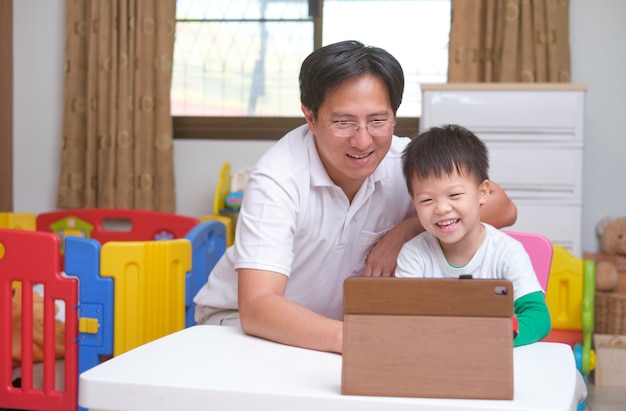 Happy Asian father and son with tablet computer are making video call to mother or relatives at home,