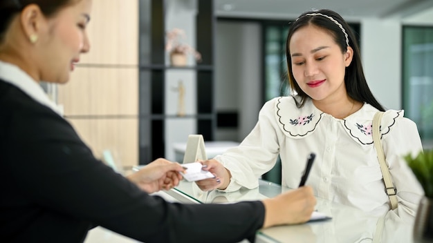 Счастливая азиатская клиентка, оплачивающая проживание кредитной картой в холле