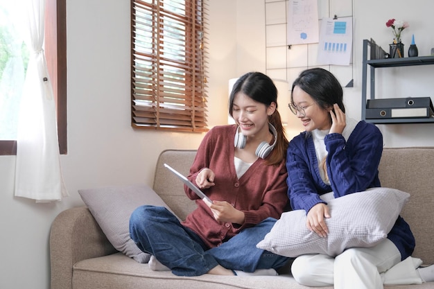 Happy asian female friends at home sitting on couch two young women with chatting on sofa gossiping and sharing secrets discussing life and relations Friendship trust concept