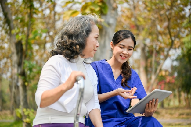 写真 幸せなアジアの女性看護師または介護士がタブレット画面で何かを老婦人に見せる