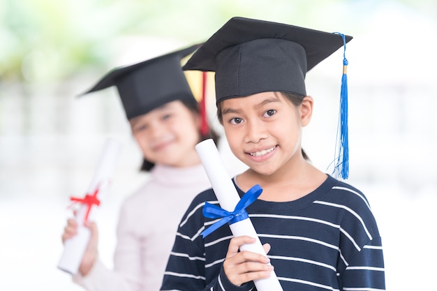 Happy asian female school kid graduates with a graduation cap
hold a rolled certificate celebrate graduation. graduation
celebration concept stock photo