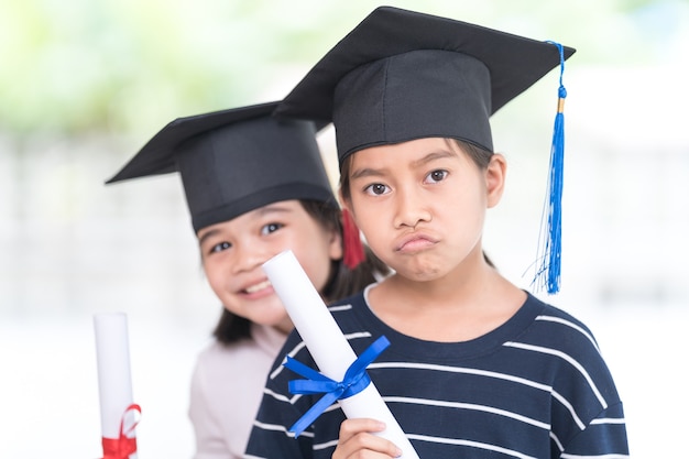 Happy Asian female school kid graduates with a graduation cap hold a rolled certificate celebrate graduation. Graduation Celebration Concept Stock Photo