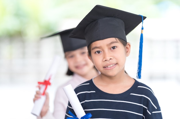 Happy asian female school kid graduates with a graduation cap\
hold a rolled certificate celebrate graduation. graduation\
celebration concept stock photo