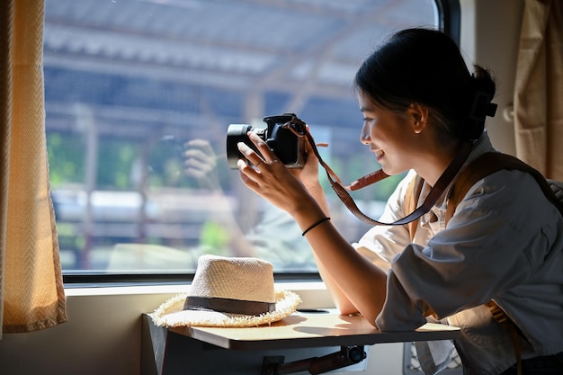 幸せなアジア人の女性旅行者が席に座り、カメラで電車から写真を撮る