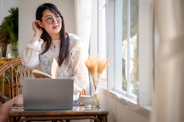 Felice di persone freelance asiatiche donna d'affari che prende appunti scritti su un notebook che lavora casualmente con un computer portatile con una tazza da caffè e uno smartphone al bar, stile di vita aziendale