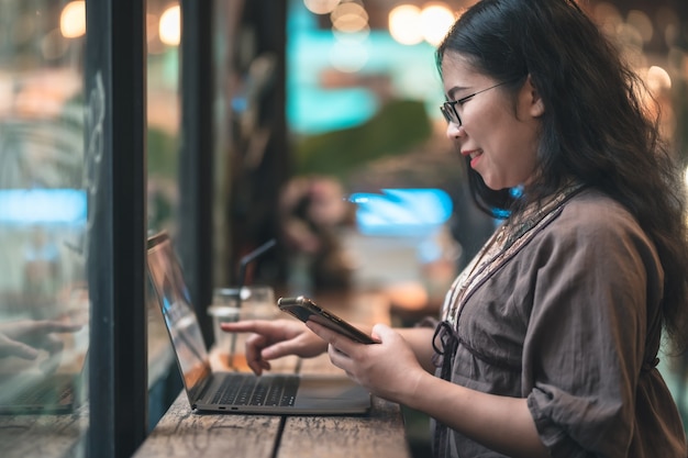 Happy of asian freelance people Businesswoman writing message on smartphone casual working with laptop computer with a coffee cup mug at the cafe,Business Lifestyle