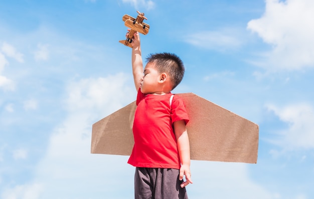 행복 한 아시아 재미 아이 또는 아이 어린 소년 미소 착용 파일럿 모자 놀이와 장난감 골판지 비행기 날개 비행 보류 비행기 장난감 야외 여름 푸른 하늘 구름, 시작 자유와 고글