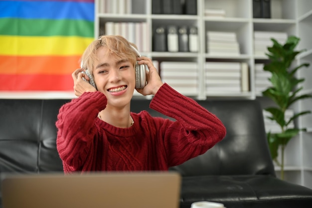 A happy Asian gay man is enjoying the music while relaxing in his apartment living room