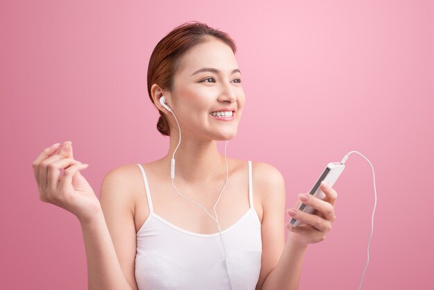 Happy asian girl dancing and listening to the music isolated on a pink background