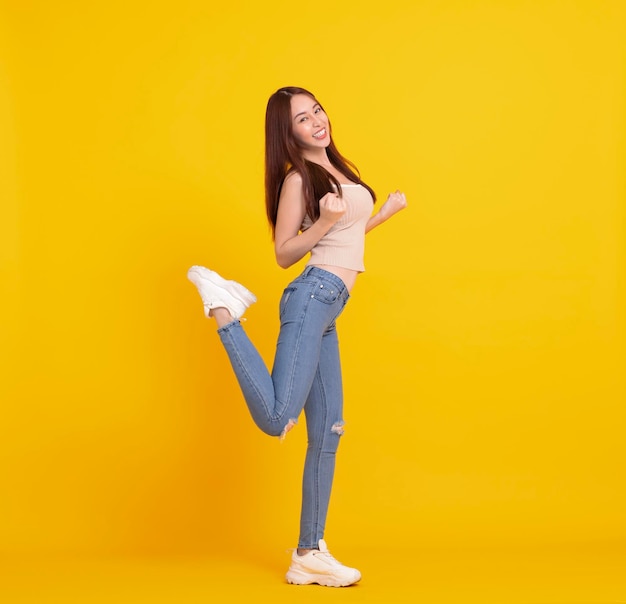 Happy Asian girl jumping and celebrating isolated over yellow