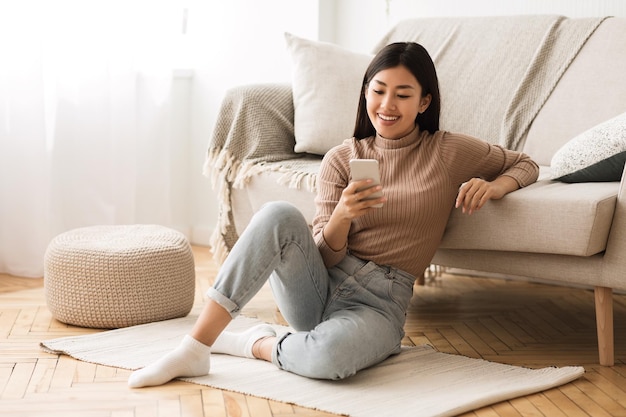 Happy asian girl messaging op de telefoon thuis