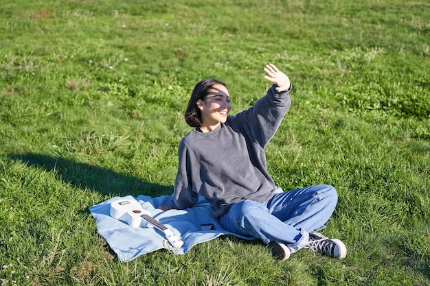 우쿨렐레와 피크닉 담요에 앉아 행복 한 아시아 소녀 손 t를 확장 하는 햇빛에서 자신을 커버