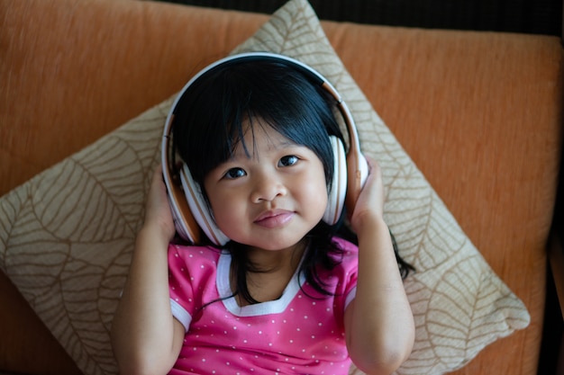 행복 한 아시아 여자 웃 고 즐기는 소파 거실에 헤드폰에서 음악을 듣는