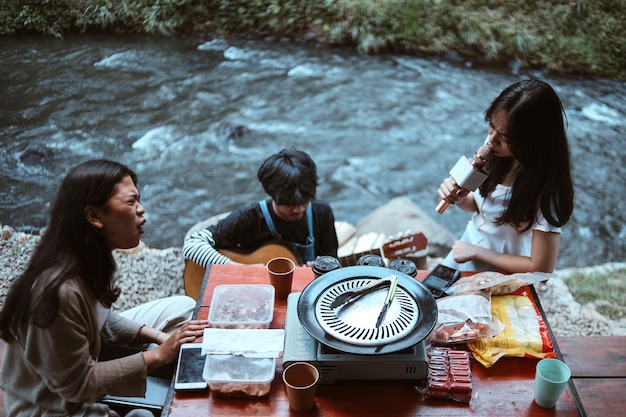 Foto ragazze asiatiche felici che cantano con il microfono con un amico che suona la chitarra al campeggio gruppo di mutieth