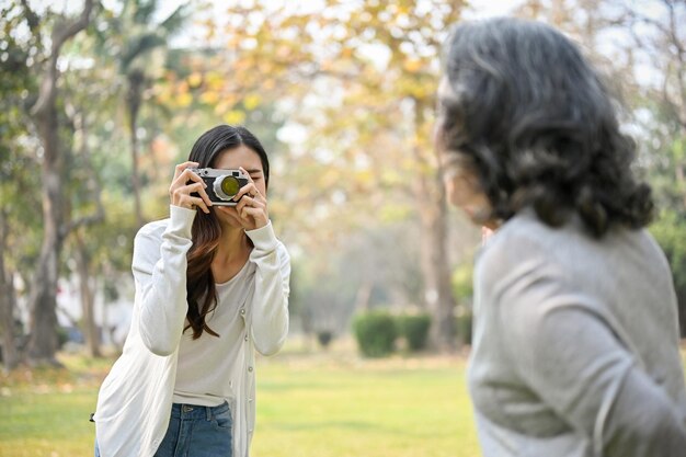 Felice nipote asiatica che scatta una foto di sua nonna con una fotocamera retrò