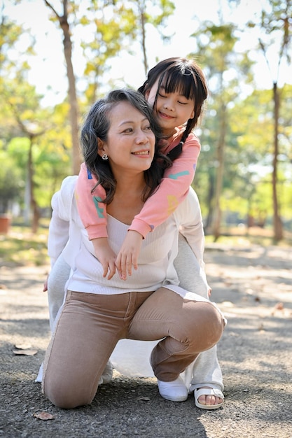 Happy Asian grandmother carrying kid hugging piggy back spending time in the park