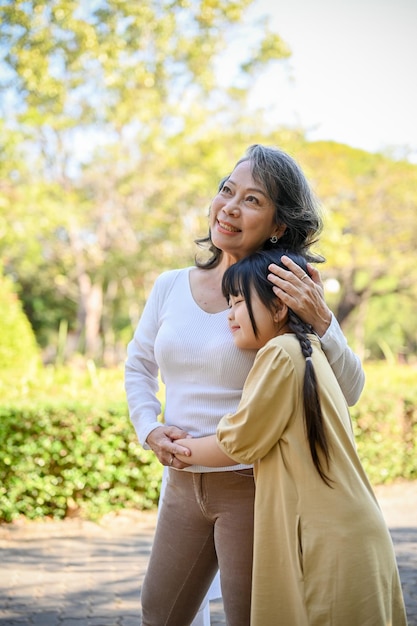 Happy Asian grandmother and lovely little granddaughter giving hug to each other