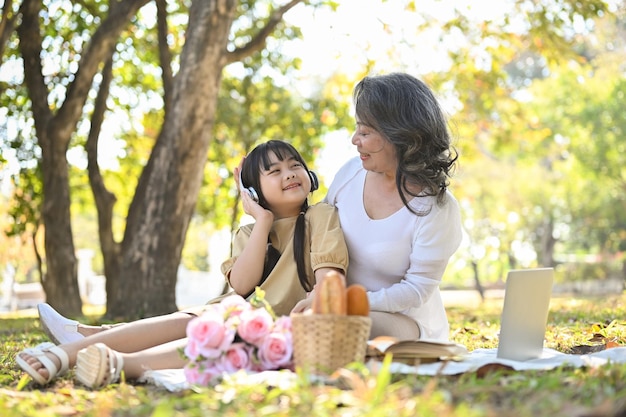 Happy Asian grandmother picnicking with her lovely granddaughter in the beautiful park