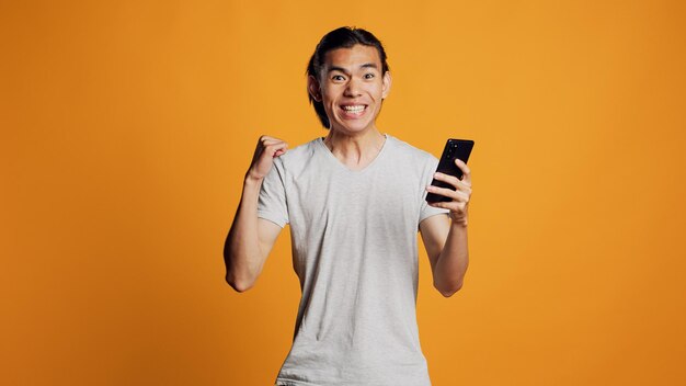 Happy asian guy browsing internet on mobile phone               person