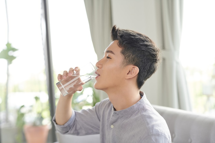 Photo 自宅でソファの飲料水に座っている幸せなアジア人の男自宅でソファの飲料水に座っている幸せなアジア人の男
