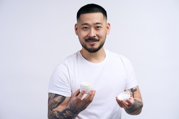 Happy asian handsome man wearing white t shirt holding cream