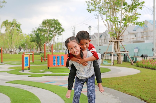 행복한 아시아 어린 소년과 소녀 아이는 정원에서 등을 타고 놀이를 하고 있습니다. 형제는 자매의 등에 타고 있습니다