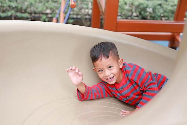 Foto ragazzino asiatico felice che si diverte mentre gioca a slider nel parco giochi