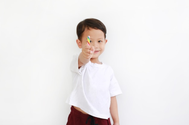 Счастливый азиатский мальчик держа конфету леденца на палочке против белой предпосылки. Сосредоточьтесь на красочном леденце в руке
