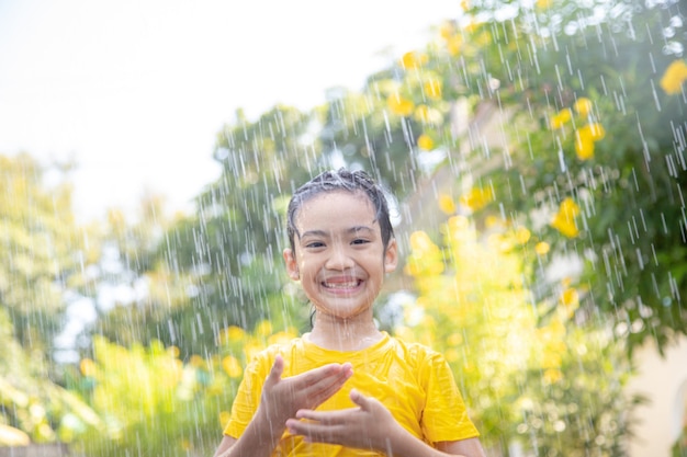 햇빛 속에서 비와 함께 즐겁게 노는 행복한 아시아 어린 소녀