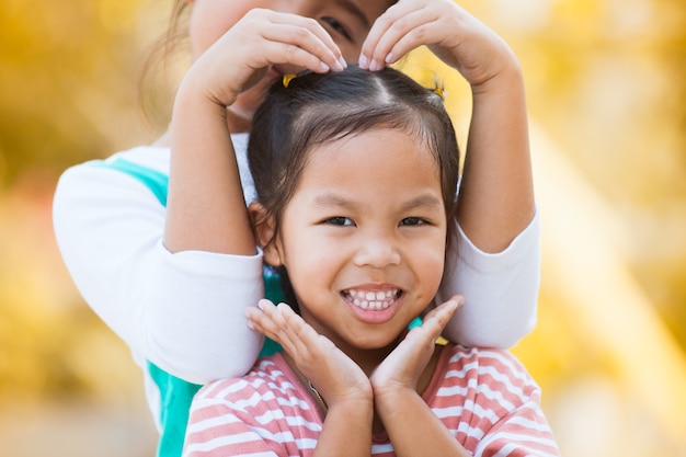 幸せなアジアの小さな子供の女の子は、愛の彼女の妹と心の形で手を作って