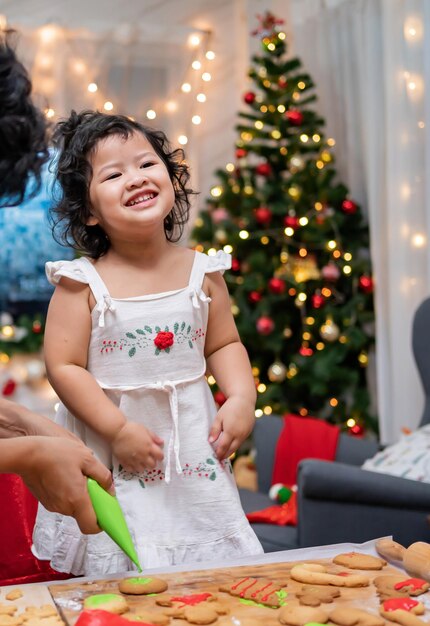 크리스마스 날 부모와 함께 집에서 진저브레드를 요리하는 행복한 아시아 소녀. 아이를 위한 수제 크리스마스 쿠키.