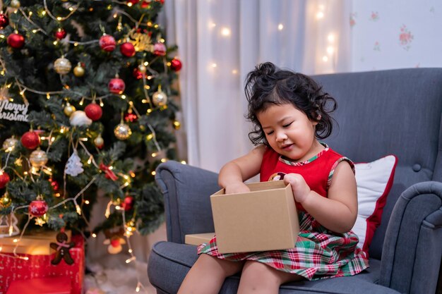 幸せなアジアの少女はクリスマスの日に楽しんでいます。休日に家でクリスマスツリーの装飾を持つ親と子供。