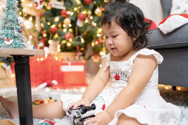 Happy Asian little girl have fun on Christmas day. Kid with parent with Christmas tree decoration at home on holiday.