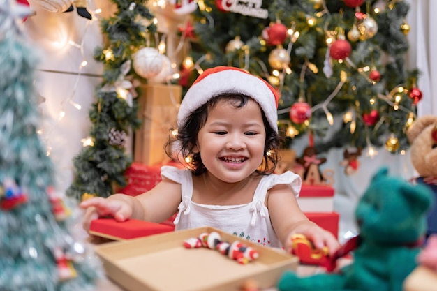 Happy Asian little girl have fun on Christmas day. Kid with parent with Christmas tree decoration at home on holiday.