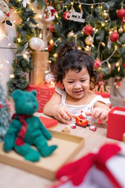 幸せなアジアの少女はクリスマスの日に楽しんでいます。休日に家でクリスマスツリーの装飾を持つ親と子供。