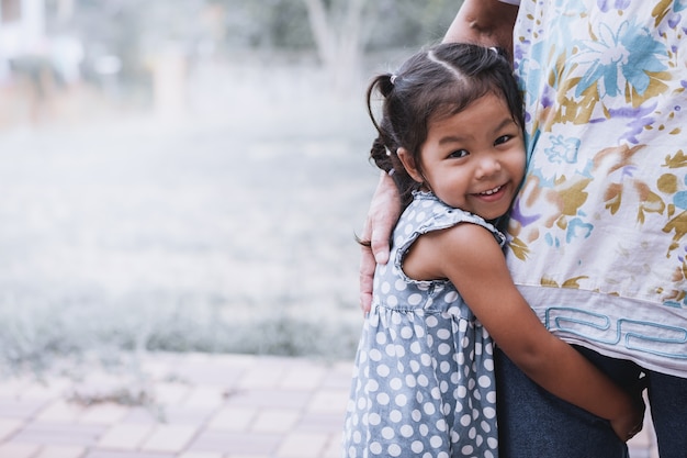 ヴィンテージの色調で彼女の母親の脚を抱擁している幸せなアジアの少女