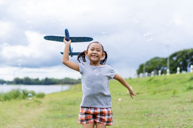 Счастливая азиатская маленькая девочка запускает воздушного змея на летнем зеленом пастбище.