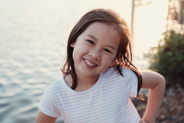 Happy Asian little girl smiling with sun flare background by the lake