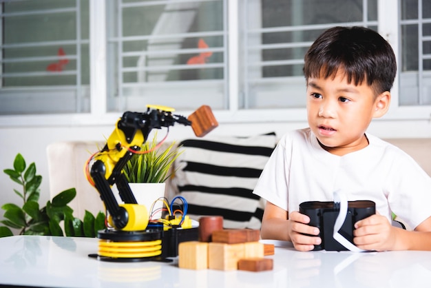 Felice ragazzino asiatico utilizzando il telecomando che gioca il braccio robotico della macchina per raccogliere il blocco di legno