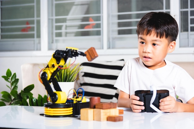 Happy Asian little kid boy using remote control playing robotic machine arm for pick up wood block